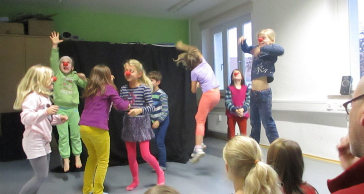 Kinder spielen Zirkus in einem Kulturhaus. Sie hüpfen und haben rote Clownsnasen aufgesetzt.