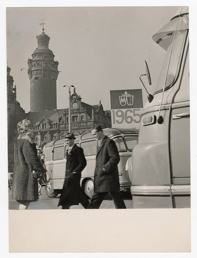 Schwarz-weiß Foto aus den 1960er Jahren mit Männern und Frauen zwischen parkenden Autos. Dahinter das Neue Rathaus mit Rathausturm.