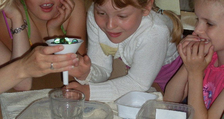 Kinder beim Experimentieren mit einem Glas und Murmeln in einem Trichter.