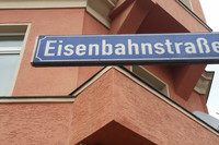 Blaues Straßenschild an der Eisenbahnstraße in Leipzig vor rotem Haus.