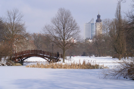 Zugefrorener Teich mit einer Brücke im Johannapark. Im Hintergrund der Turm des Neuen Rathauses und das City-Hochhaus.