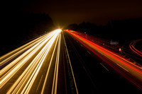 Langzeitaufnahme einer Autobahn bei Nacht. Durch die lange Belichtungszeit sieht man statt vorbeifahrender Autos nur Lichtstreifen von deren Scheinwerfern