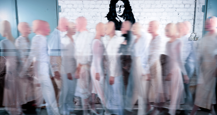 Schablonenbild von Leibniz an einer weißen Ziegelsteinwand. Davor laufen viel futuristische Figuren, die halb durchsichtig sind.