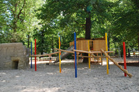 Klettermöglichkeiten und ein Baumhaus mit Rutsche unter einem großen Baum auf dem Spielplatz am Rennbahnweg