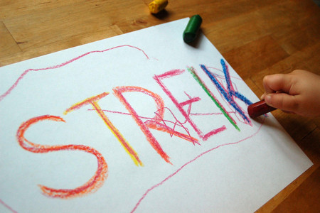 Ein Kind malt mit Wachskreide das Wort Streik auf ein Blatt Papier