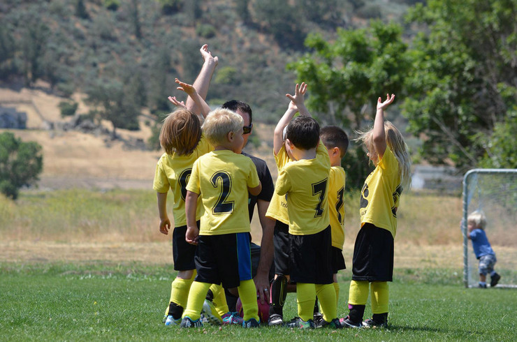 Eine Fußballmannschaft aus kleinen Kindern steht im Kreis, man sieht sie von hinten. 