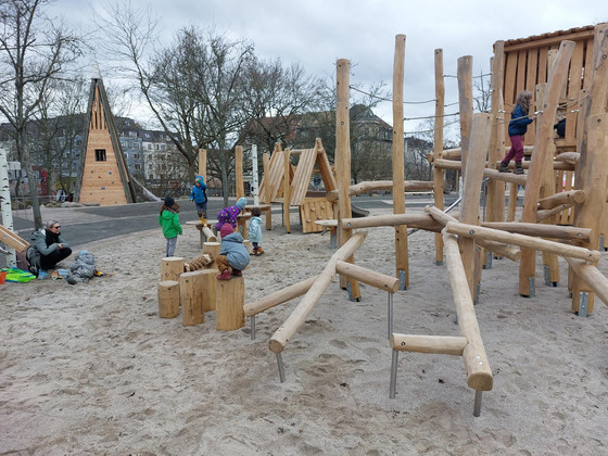 Auf einem Spielplatz mit neuen Spielgeräten aus Holz klettern kleine Kinder.