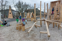 Auf einem Spielplatz mit neuen Spielgeräten aus Holz klettern kleine Kinder.