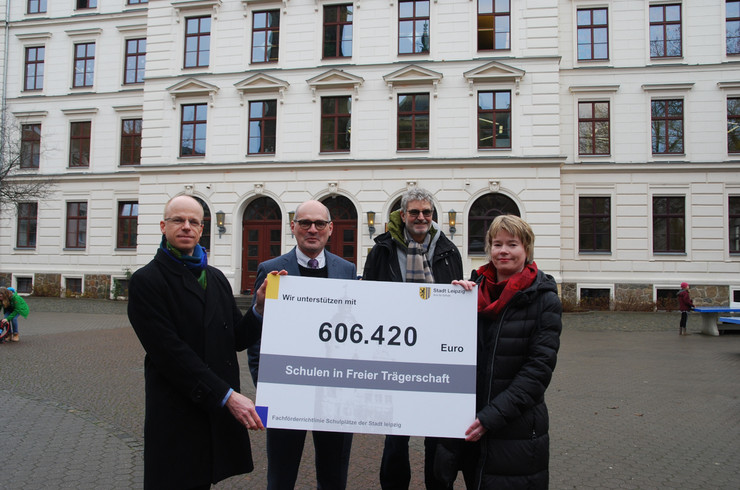 Drei Männer und eine Frau halten eine große Tafel mit der Aufschrift "Wir unterstützen mit 606.420 Euro Schulen in freier Trägerschaft"