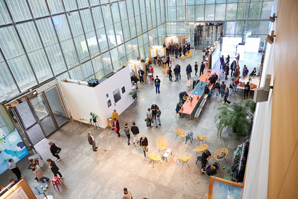 Blick von oben in eine große Halle mit Ausstellungsflächen und Tischen und Menschen im Gespräch