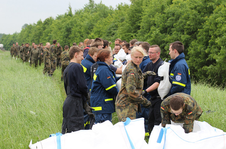 Helfer von Bundeswehr, Technischem Hilfswerk und Feuerwehr sichern einen Deich mit Sandsäcken