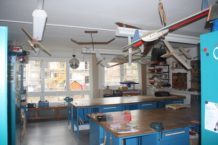 Über mehreren Werkbänken hängen Modellflugzeuge aus Holz. An den Wänden ist diverses Werkzeug angebracht.