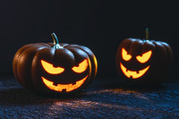 Zwei leuchtende Halloween-Kürbisse mit bösen Gesichtern vor schwarzem Hintergrund.