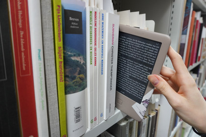 Bücherregal, eine Hand nimmt ein E-Book aus dem Regal 