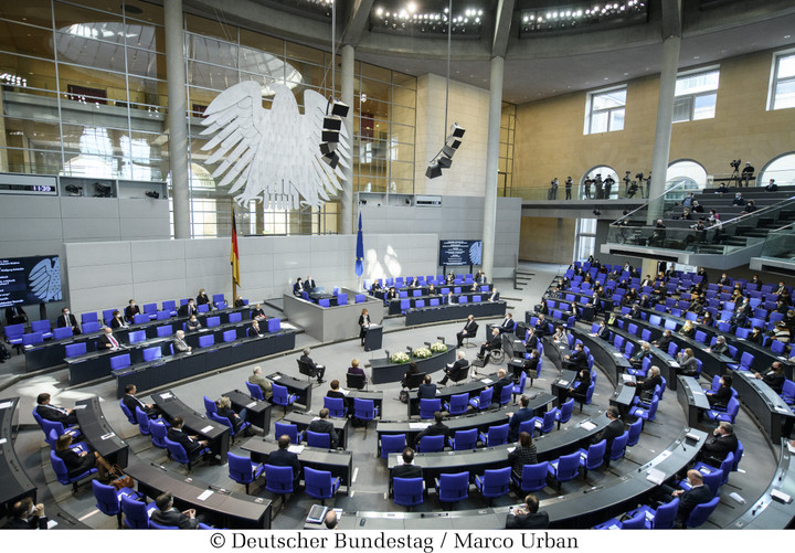 Der Sitzungs-Saal vom Bundestag von oben. Die Sitze und Tische sind im Halbkreis angeordnet. An der Stirnseite hängt der Bundesadler