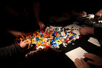 Viele Legoteile auf einem Tisch, Hände greifen nach den Teilen.