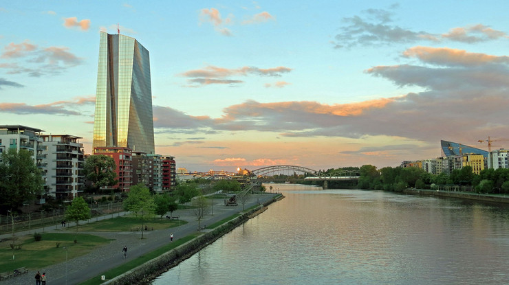 Das Hochhaus der Europäischen Zentralbank in Frankfurt während der Abenddämmerung. Ein Glashochhaus, welches das untergehende Sonnenlicht reflektiert.