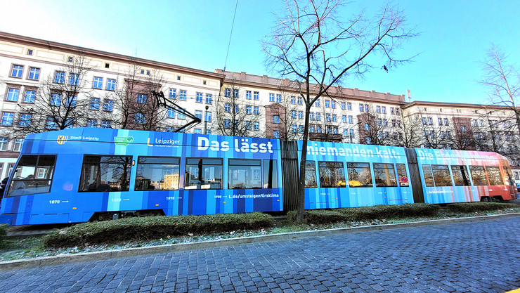 Eine Straßenbahn mit Klimastreifen-Beklebung auf Schienen mit dem Leipziger Neuen Rathaus im Hintergrund.