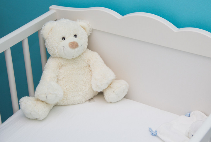 ein weißer Teddybär sitzt in der Ecke eines Gitterbetts.
