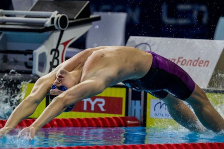 Sportschwimmer Marek Ulrich bei Start im Rückenschwimmen. Er springt gestreckt aus dem Wasser heraus nach hinten.