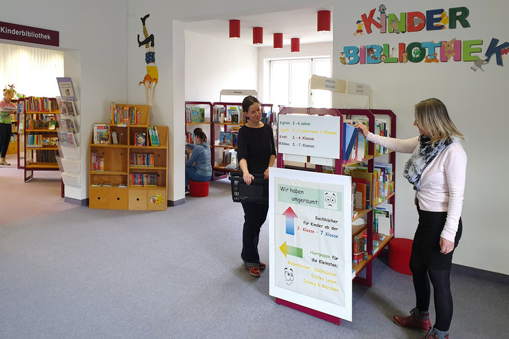 Ein paar Besucherinnen und Regale mit Büchern in der Kinderbibliothek