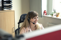 Eine Mitarbeiterin des Bürgertelefons sitzt mit Headset vor dem Computer und berät eine Anruferin/einen Anrufer.
