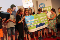 Einige Kinder der Erich-Zeigner-Schule stehen auf einer Bühne und nehmen die Auszeichnung „Schule der Toleranz“ sowie einen großen Scheck über 500 Euro entgegen.