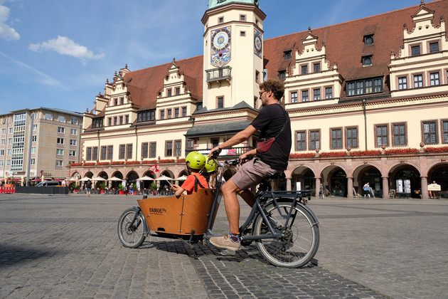 Auf dem Leipziger Marktplatz fährt ein Mann in einem Lastenrad, in dem zwei Kinder sitzen