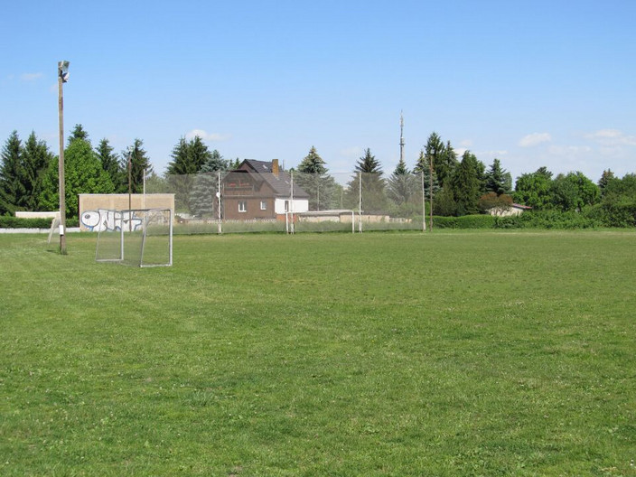 Rasenspielfläche des Erich-Steinfurth-Stadion. Hinter dem Spielfeld steht ein Einfamilienhaus.