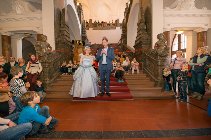 Umringt von großen und kleinen Gästen des Familienspielefestes begrüßt der Oberbürgermeister auf der Treppe zur Oberen Wandelhalle die Anwesenden. An seiner Seite eine Prinzessin in einem hellblauen Kleid.