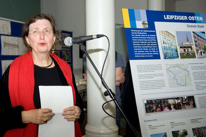 Die Baubürgermeisterin steht vor einem Mikrophon mit einem Blatt Papier in den Händen. Neben ihr eine steht eine Infotafel zum Leipziger Osten.