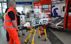 Zwei Rettungssanitäter (Mann und Frau) schieben eine rollbaren Babyinkubator in einen Rettungswagen während einer Vorführung