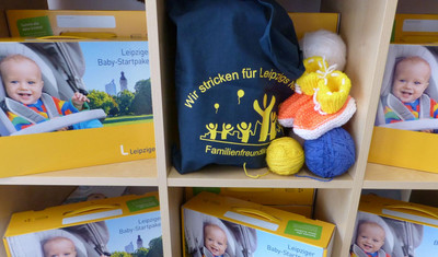 Mehrere Leipziger Babystartpakete mit Stricksachen in Fächern eines Regals angeordnet.