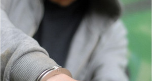Ein junger Mann mit tief ins Gesicht gezogener Kapuze und den Händen in Handschellen