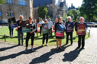Mehrere Menschen stehen mit Plakaten in der Hand auf einer Wiese unweit der Thomaskirhche