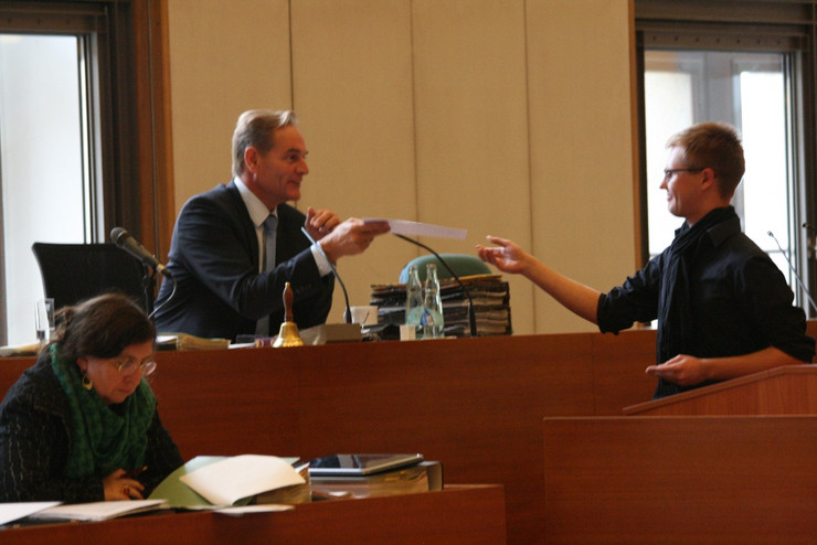 Ein junger Mann in schwarzem Hemd und mit schwarzem Schal übergibt dem sitzenden Oberbürgermeister Burkhard Jung ein Schriftstück