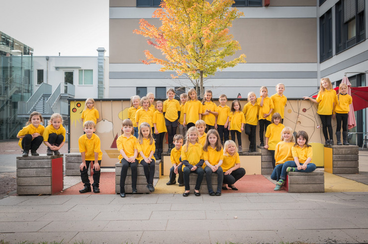 Viele Kinder des Spatzenchores der Schola Cantorum in gelben T-Shirts auf einem Schulhof