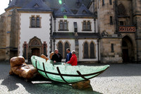 In der Bildmitte steht ein gläsernes Boot, die sogenannte Glasarche, welche aus einer großen Holzhand gleitet.