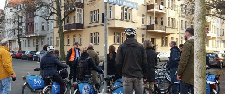 Mehrere Fahrradfahrer stehen am Straßenrand und hören einem Mann in Warnweste zu.