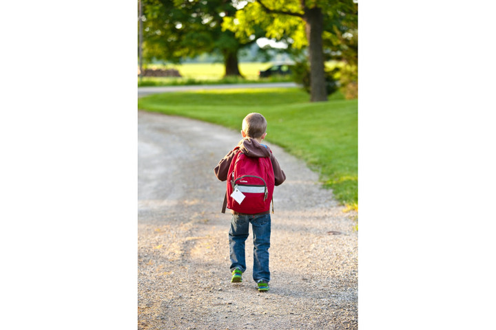 Kind mit Rucksack von hinten auf einem Schotterweg