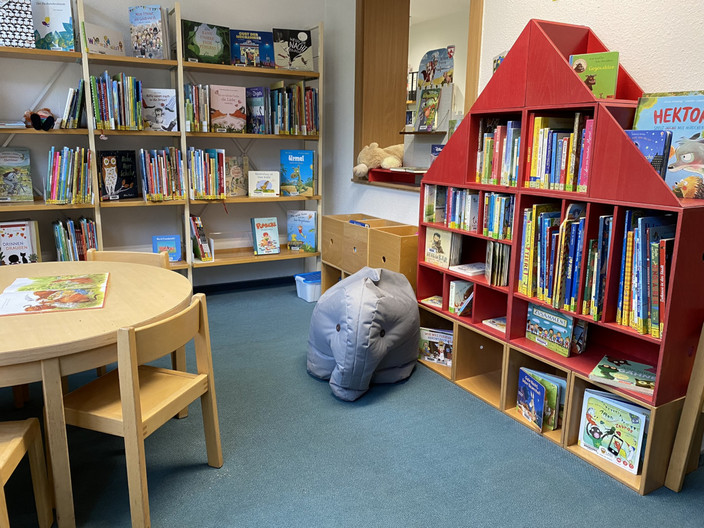 Ein rotes Holzklotz-Regal mit Kinderbüchern samt grauem Kuschel-Elefanten.