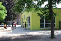 Kinder spielen vor einem hellgrünen, einstöckigen Gebäude