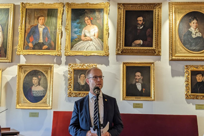 Zu sehen ist Clemens Schülke, Wirtschaftsbürgermeister der Stadt Leipzig, bei einer Rede vor einer Wand mit vielen historischen Porträts anlässlich einer Delegationsreise nach Krakau