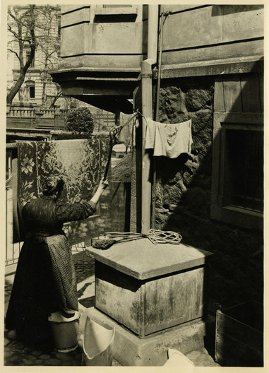 Schwarz-Weiß-Foto um 1905: Ein Frau klopft einen Teppich neben dem Ponitowski-Gedenkstein am ehemaligen Standort im Hinterhof der heutigen Gottschedstraße.