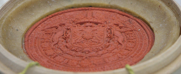 Rotes Wachssiegel mit Wappenprägung einer Urkunde in einer Holzschatulle