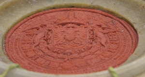 Rotes Wachssiegel mit Wappenprägung einer Urkunde in einer Holzschatulle