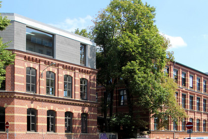 Ein historisches zweigeschossiges Kontorhaus aus roten Ziegeln wurde um einen modernen grauen Aufsatz mit großem Fenster ergänzt.