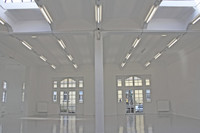 Blick in eine leere Halle mit weißen Wänden und weißen Türen, die sich im Boden spiegeln