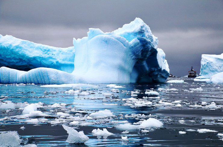 Zwischen zwei mächtigen Eisbergen manovriert sich ein kleines Forschungsboot durch Eisschollen