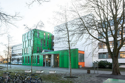 Gebäude der Franz Mehring Schule. Auffälliger grüner Eingangsbereich und mehrstöckiges Gebäude mit vielen Fensterflächen.